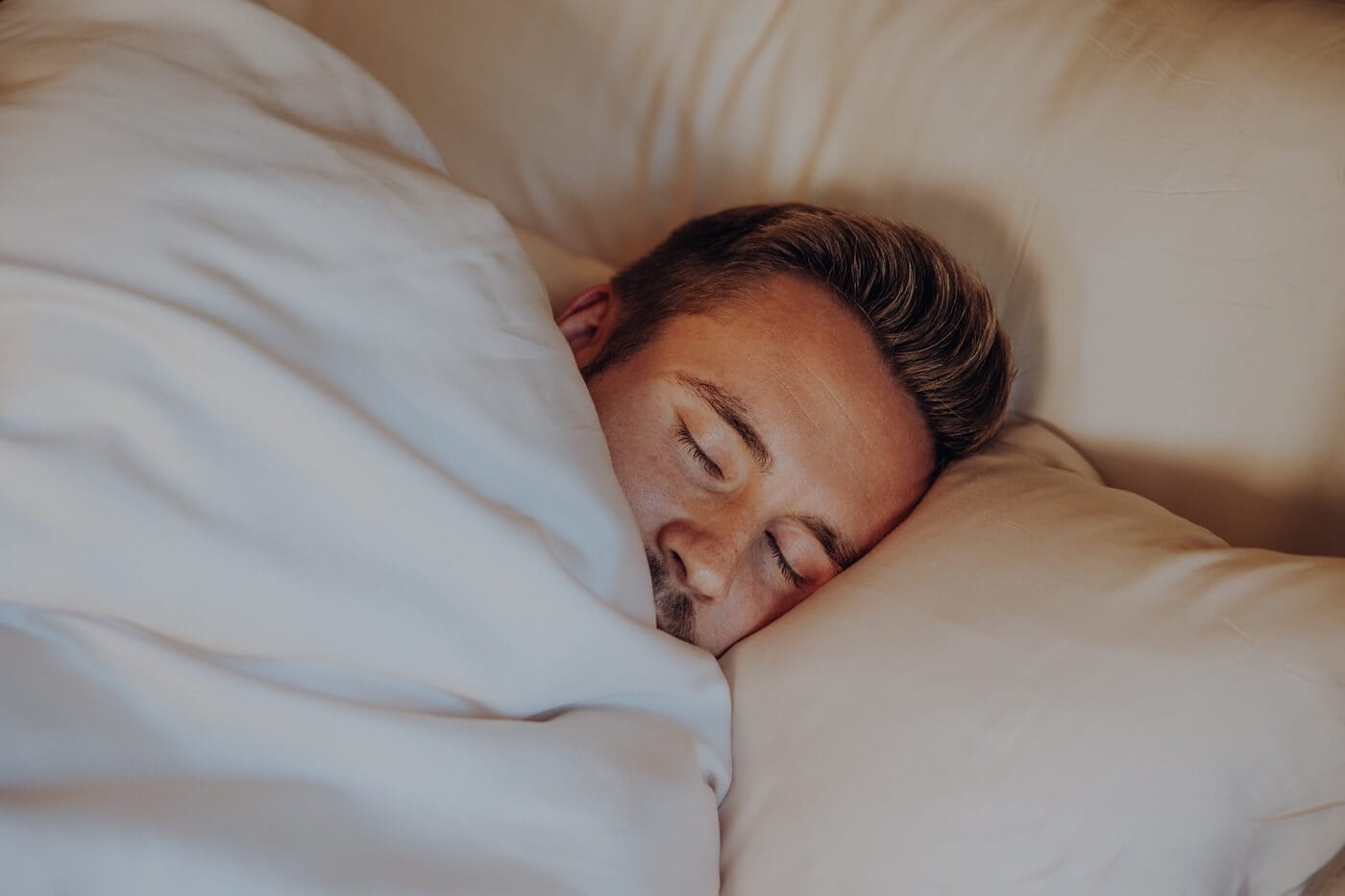 Schlafender Mann liegt ruhig im Bett und schläft tief – Darstellung von Entspannung und erholsamem Schlaf mit Ayurveda Ritualen.